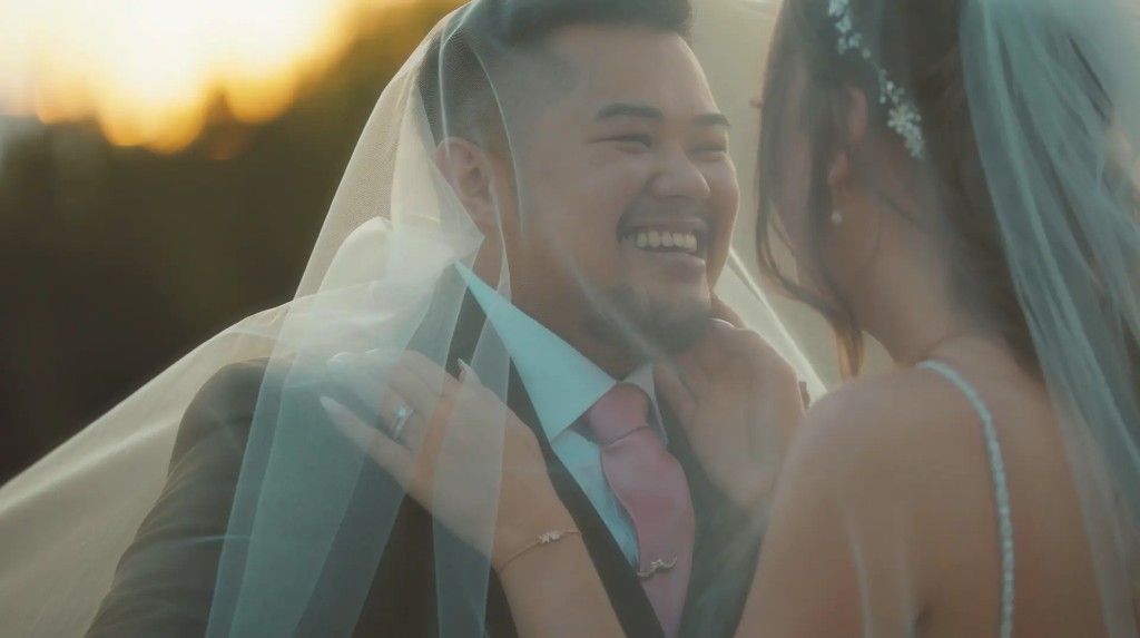 Bride and groom beneath a sheer veil, laughing together in warm sunset light—still from a Leviathan Film wedding